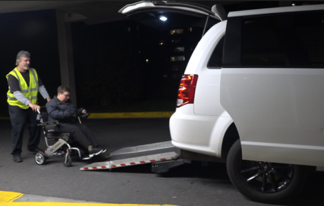 Wheelchair user Kelly Mack being helped into a wheelchair accessible Uber via a back door ramp